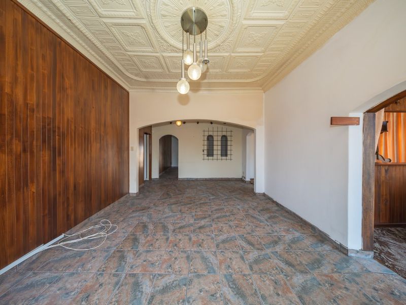 Spacious living area featuring a decorative pressed metal ceiling, timber wall paneling, and ceramic floor tiles, leading through an archway to adjacent rooms.