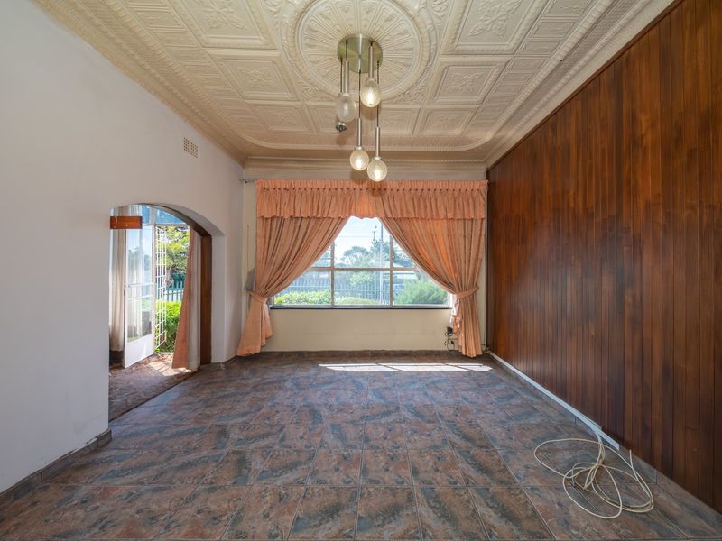 Spacious living area featuring a unique ornate pressed metal ceiling, wood-paneled feature wall, and tiled flooring with direct access to the garden.