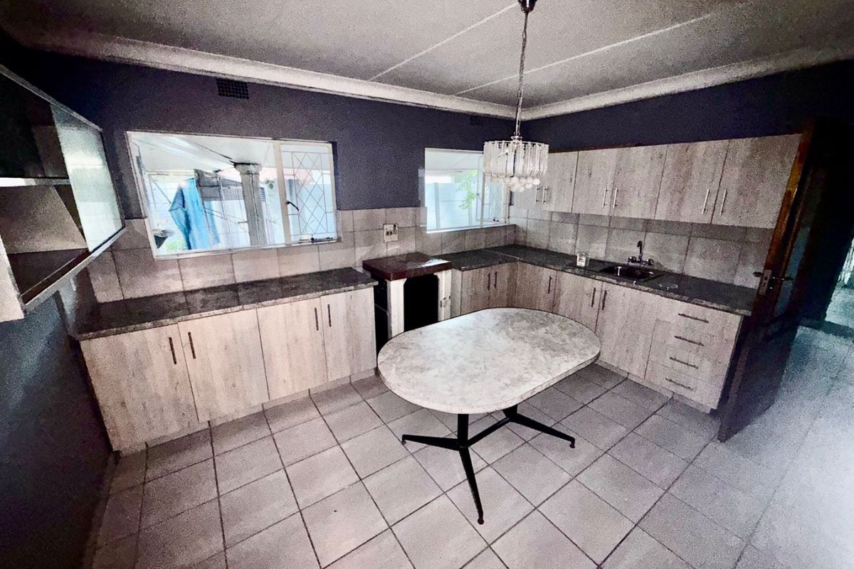 A functional kitchen featuring light wood-look cabinetry, stone-effect countertops, tiled flooring, and a tiled backsplash, offering a practical layout for daily use.
