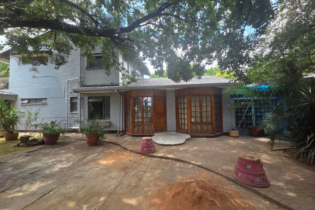 Rear exterior view of a two-story house featuring a brick paved patio area and timber-framed bay windows under mature tree canopy.