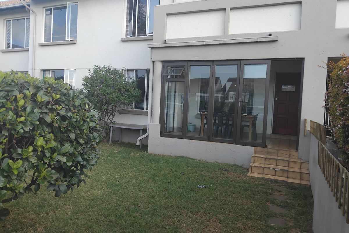 Rear view of the apartment featuring a small garden, tiled entrance steps, and an enclosed patio area with aluminium framed doors and windows.