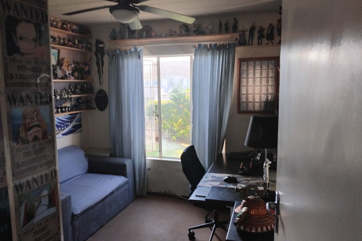 A bedroom featuring a ceiling fan and built-in shelving, currently utilized as a multi-purpose living and workspace area.
