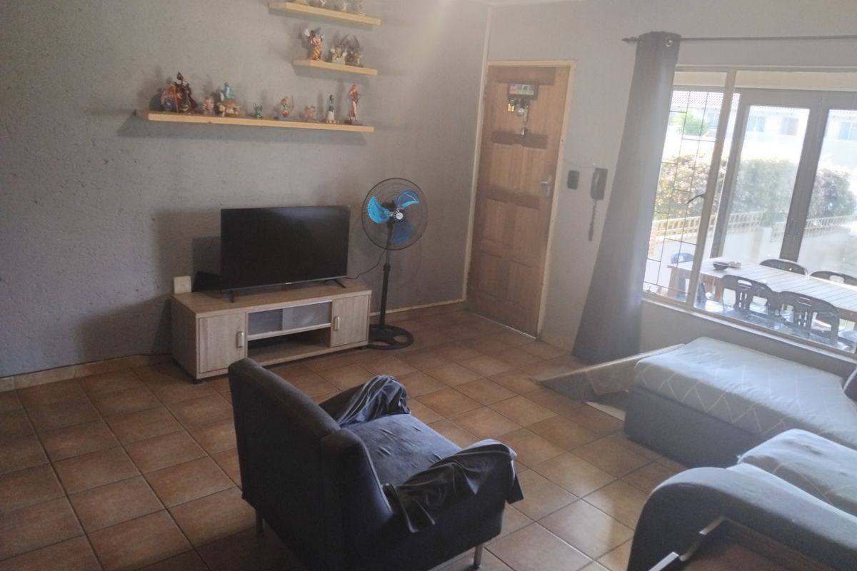 A living room featuring tiled flooring, a timber entrance door, and a large sliding glass door providing natural light and access to the exterior.