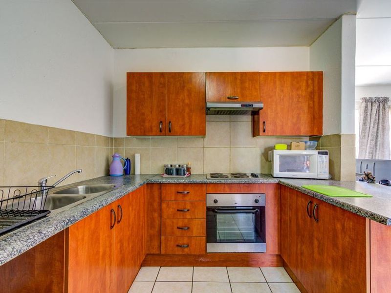 A functional kitchen featuring wood-look cabinetry, granite-style countertops, a built-in oven with hob, and a tiled backsplash.