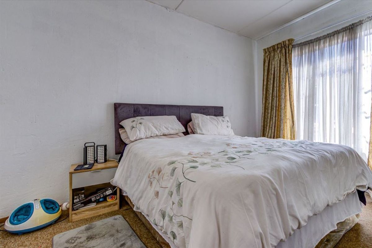 A bedroom featuring carpet flooring and large windows with curtain tracks, requiring cosmetic updates to the wall finishes and flooring.