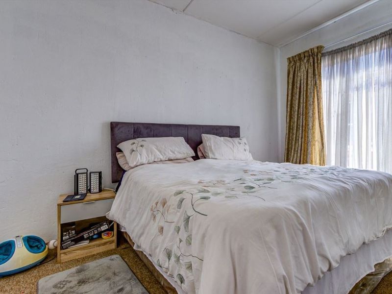 A bedroom featuring carpet flooring and large windows with curtain tracks, requiring cosmetic updates to the wall finishes and flooring.