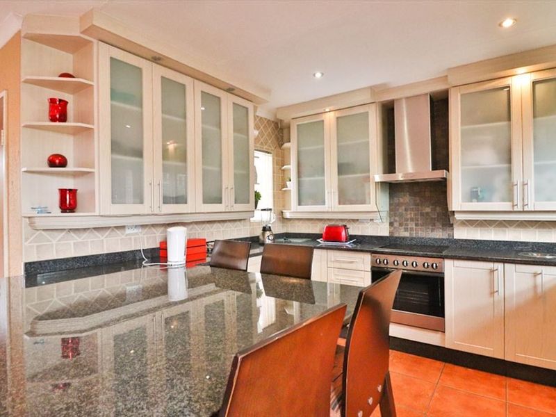 A well-appointed kitchen featuring granite countertops, built-in oven, extractor fan, and ample cabinetry with glass-fronted display units.