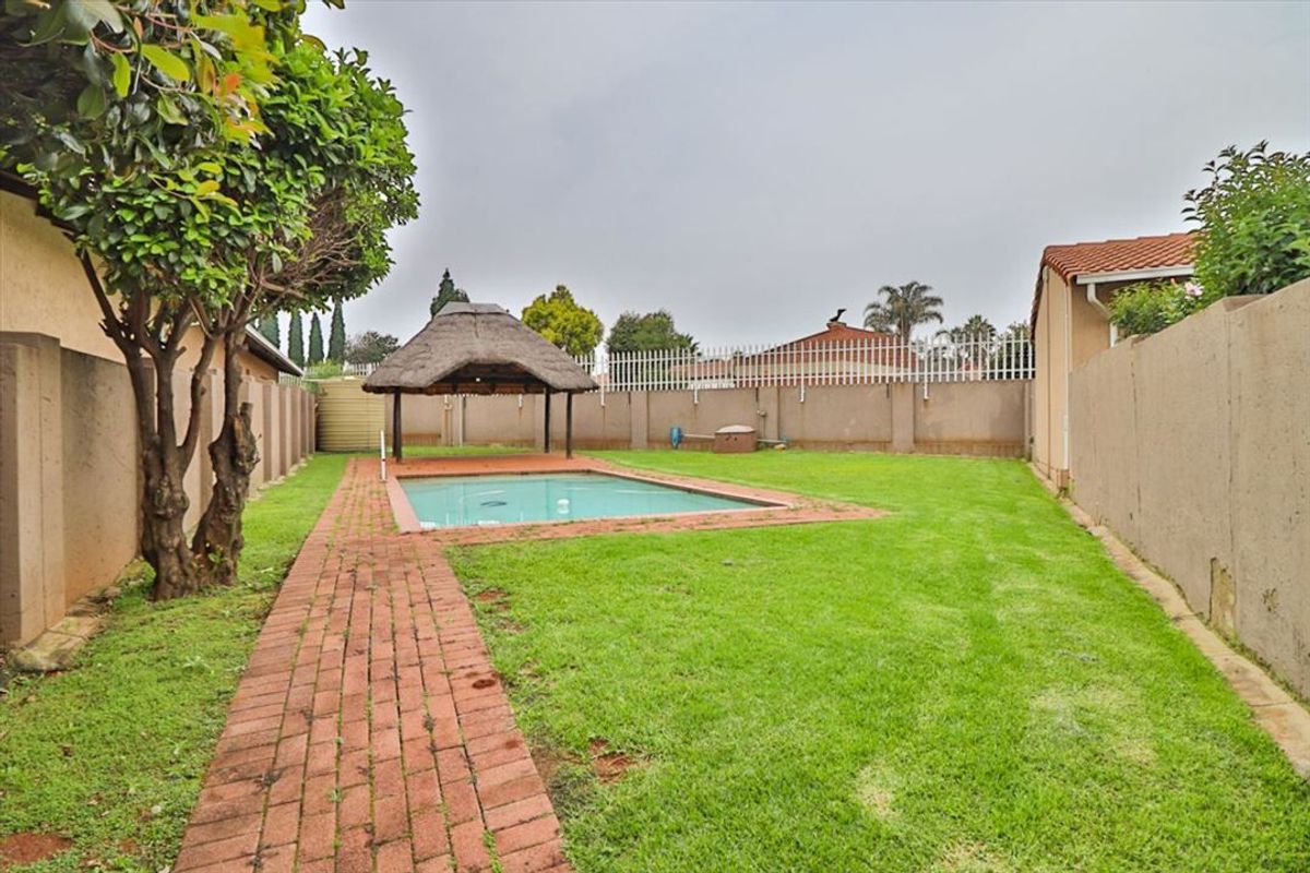 Private backyard featuring a swimming pool, a traditional thatch lapa, brick paved pathways, and a secure perimeter wall.