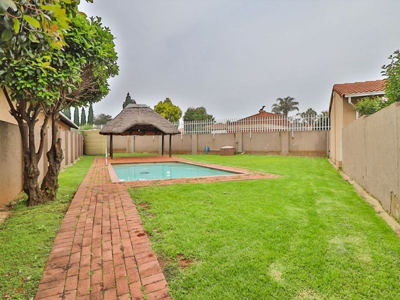 Private backyard featuring a swimming pool, a traditional thatch lapa, brick paved pathways, and a secure perimeter wall.