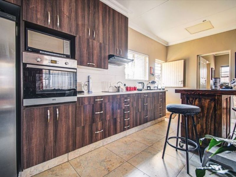 A functional kitchen featuring dark wood-grain cabinetry, built-in oven and microwave, tiled flooring, and a breakfast counter.