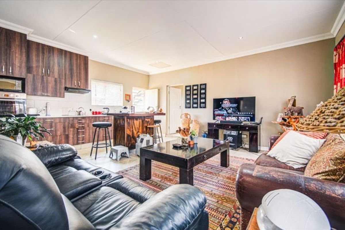 Open-plan living area featuring a modern kitchen with dark wood cabinetry, a central island, and integrated appliances, flowing into a comfortable lounge space.