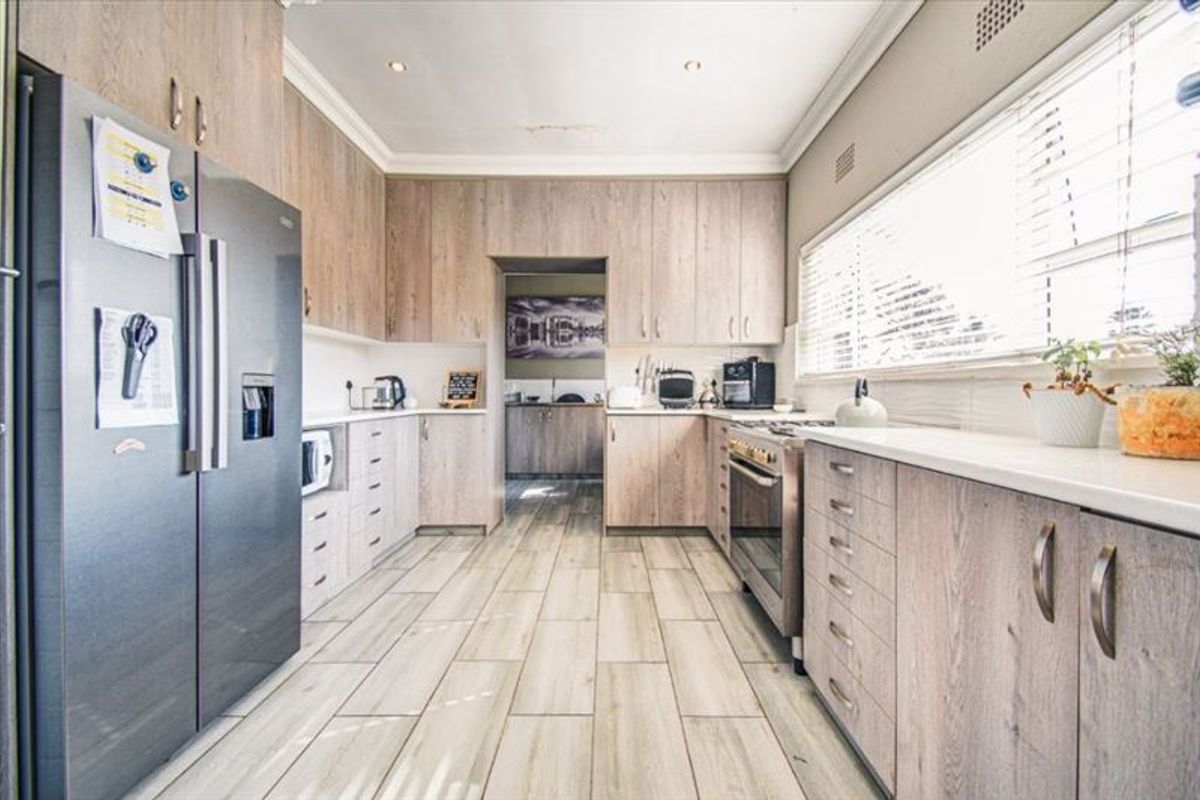 A well-appointed kitchen featuring light wood-grain cabinetry, stone countertops, a freestanding oven, and tiled flooring, with a convenient adjoining scullery area.