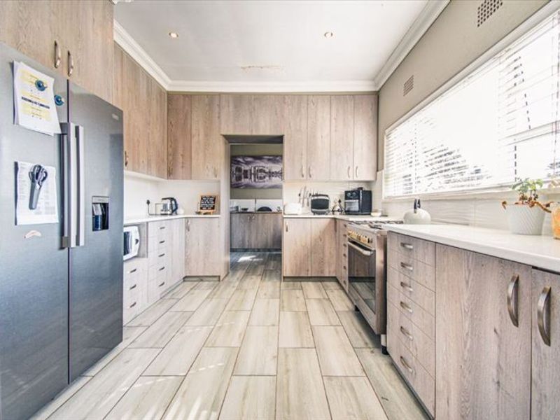 A well-appointed kitchen featuring light wood-grain cabinetry, stone countertops, a freestanding oven, and tiled flooring, with a convenient adjoining scullery area.