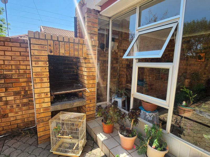 Outdoor patio area featuring a built-in brick braai, paved flooring, and large glass windows providing natural light to the adjacent interior space.