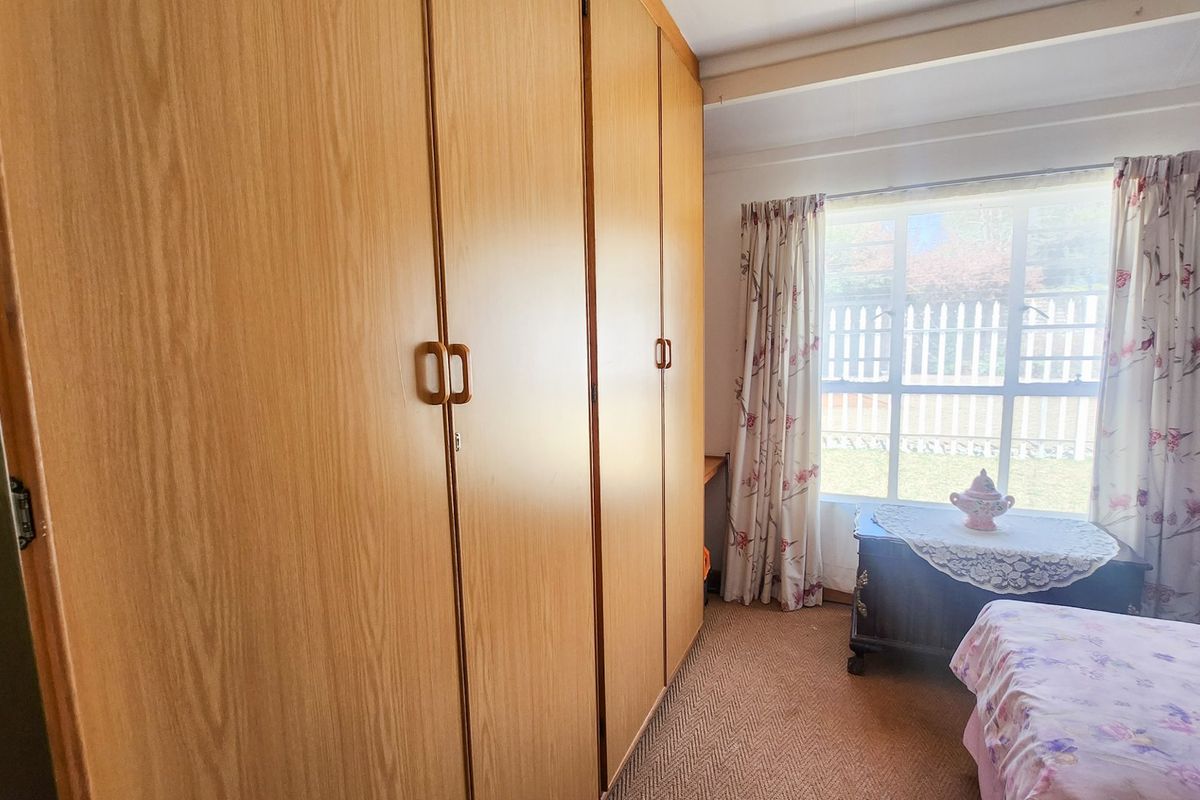 A bedroom featuring floor-to-ceiling built-in wooden cupboards and a large window providing natural light.