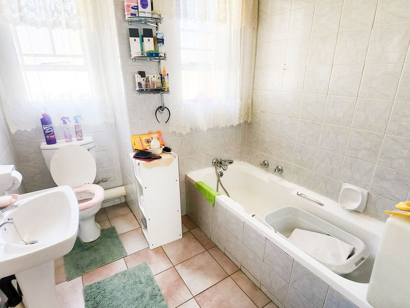 A functional bathroom featuring a pedestal basin, toilet, and bathtub with tiled finishes, offering a dated aesthetic ready for modernization.