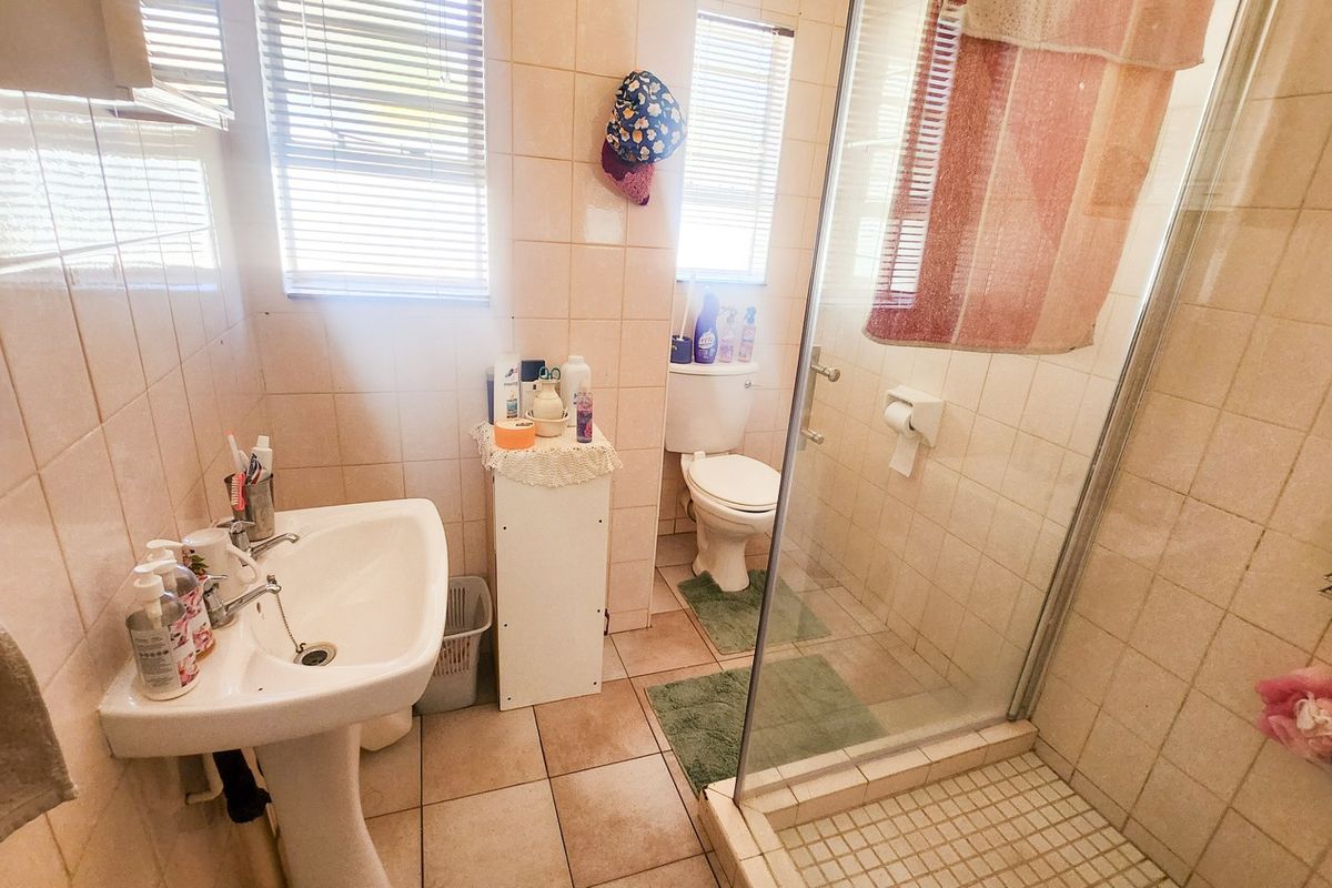 A functional bathroom featuring a pedestal sink, a glass-enclosed shower, and a toilet, finished with neutral wall and floor tiles.