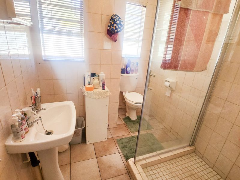 A functional bathroom featuring a pedestal sink, a glass-enclosed shower, and a toilet, finished with neutral wall and floor tiles.