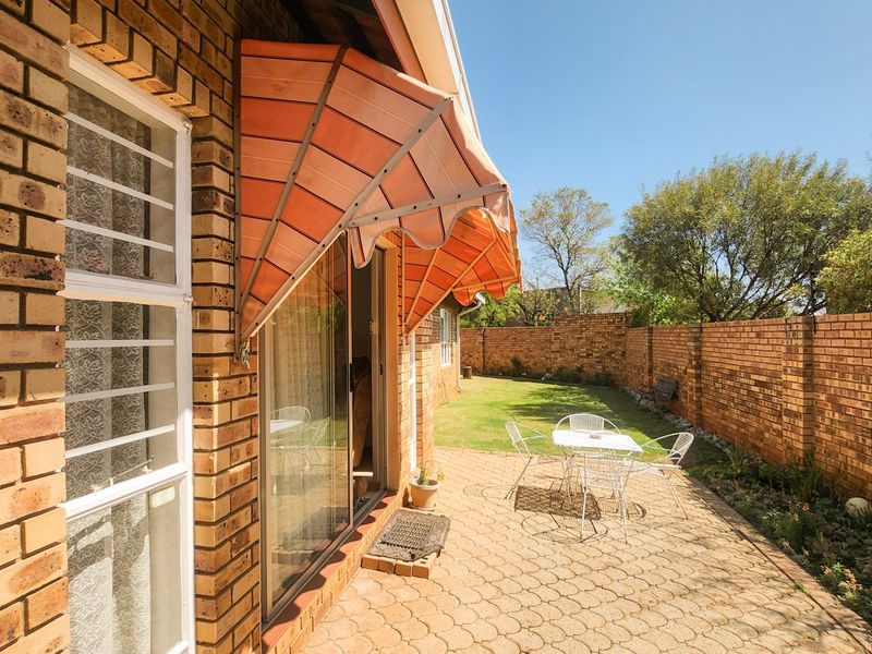 Rear exterior view of the townhouse featuring a paved patio area, face brick walls, and a retractable awning over the sliding glass door.