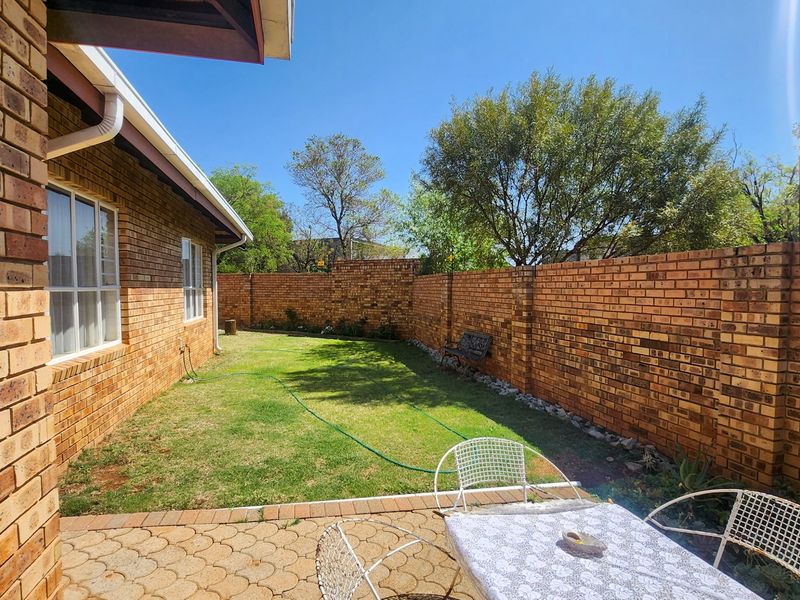 A private rear garden featuring a paved patio area, a well-maintained lawn, and secure brick boundary walls.