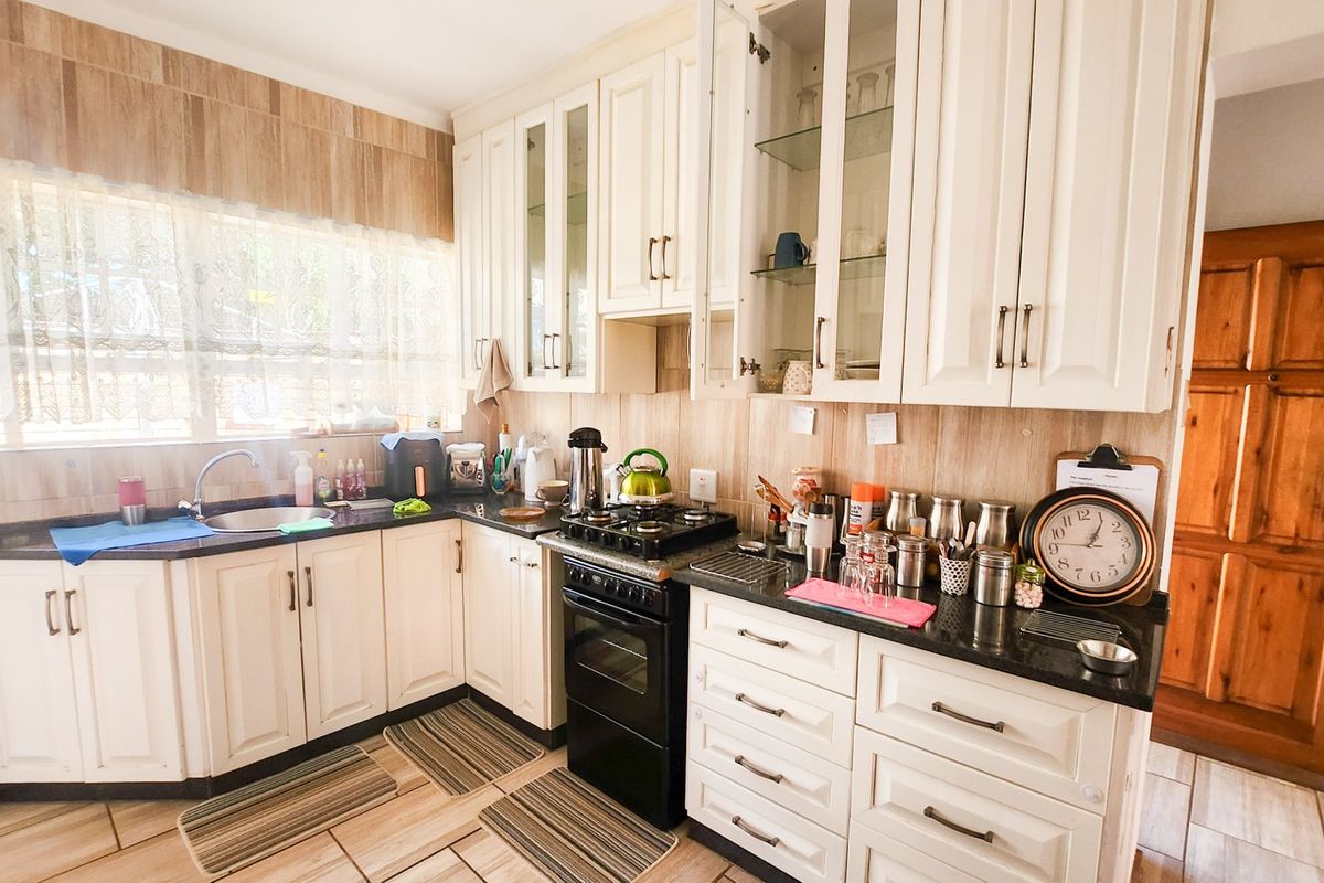A functional kitchen featuring white cabinetry, granite countertops, a gas hob with oven, and tiled finishes throughout.