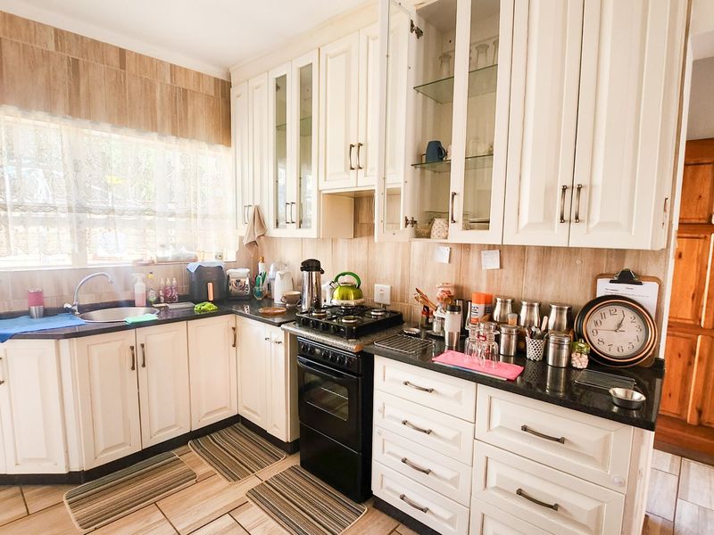 A functional kitchen featuring white cabinetry, granite countertops, a gas hob with oven, and tiled finishes throughout.