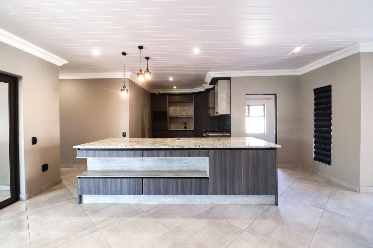 Modern kitchen featuring a large central island with stone countertops, sleek built-in cabinetry, and contemporary pendant lighting in an open-plan layout.
