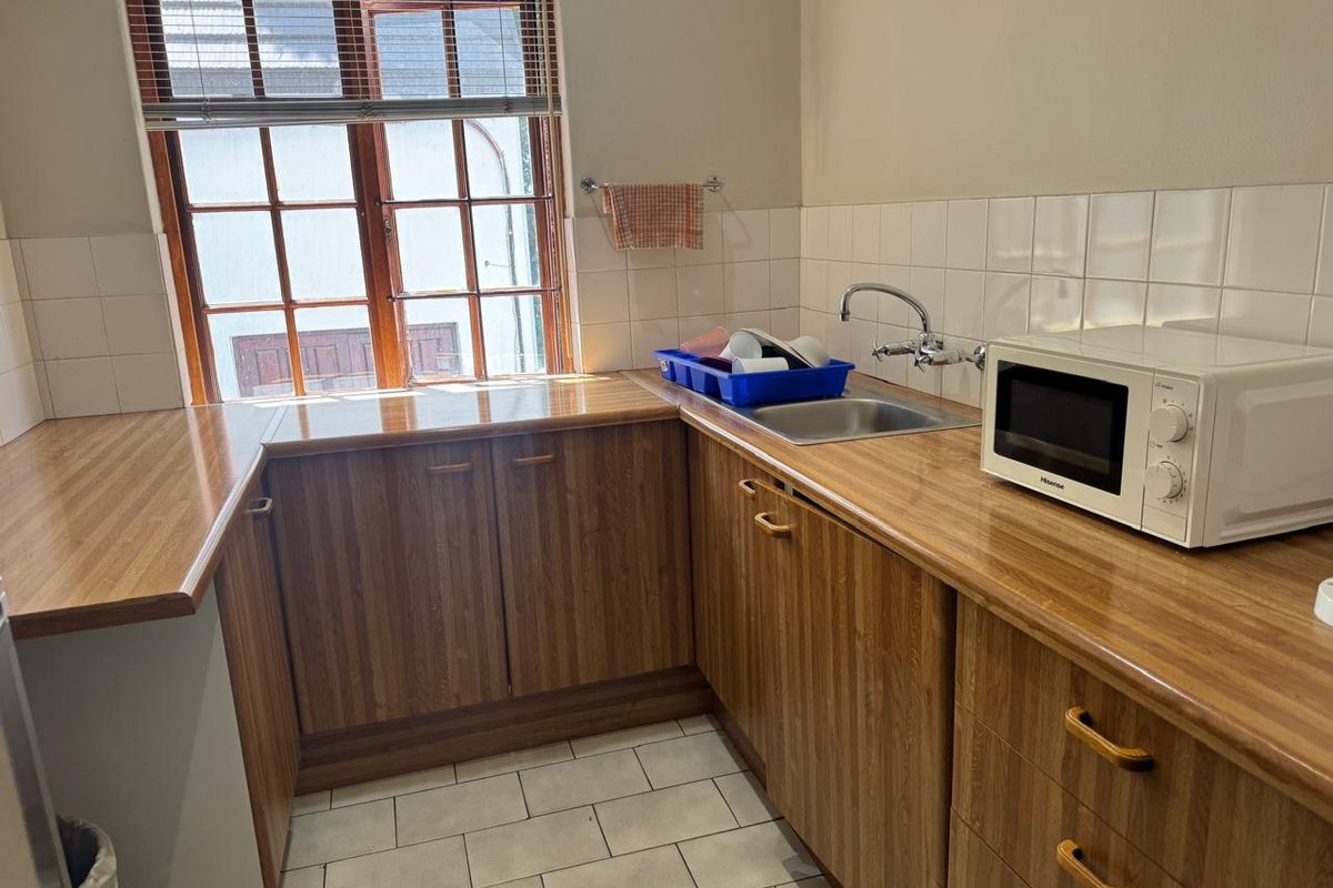 A functional kitchen featuring wood-grain cabinetry, laminate countertops, a stainless steel sink, and tiled finishes, providing a practical workspace.