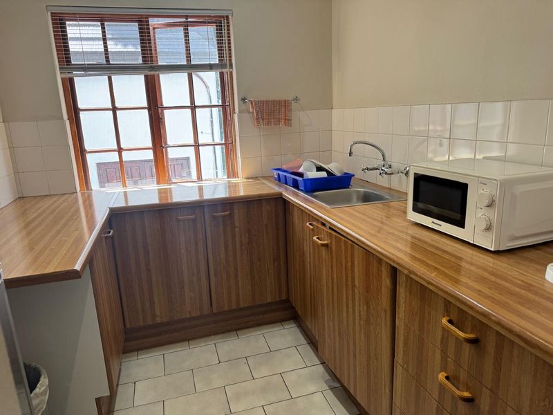 A functional kitchen featuring wood-grain cabinetry, laminate countertops, a stainless steel sink, and tiled finishes, providing a practical workspace.
