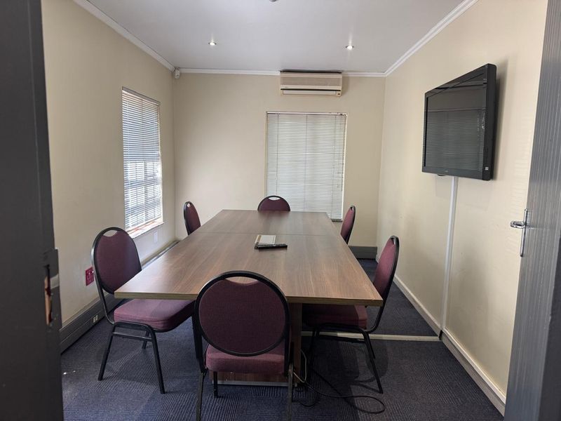 A functional office meeting room featuring wall-mounted air conditioning, a television, venetian blinds, and carpeted flooring, suitable for professional use.