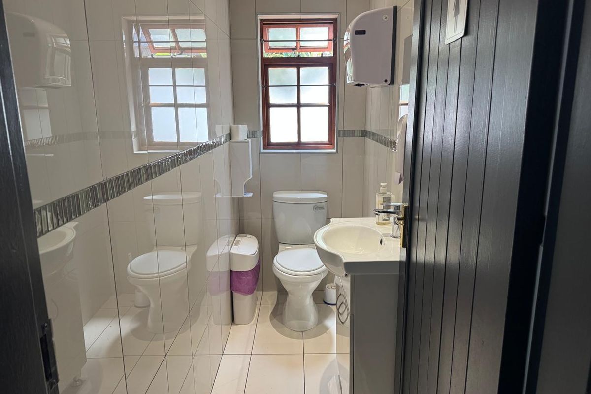 A compact, well-maintained commercial bathroom featuring tiled walls, a pedestal vanity with a washbasin, and a standard toilet.