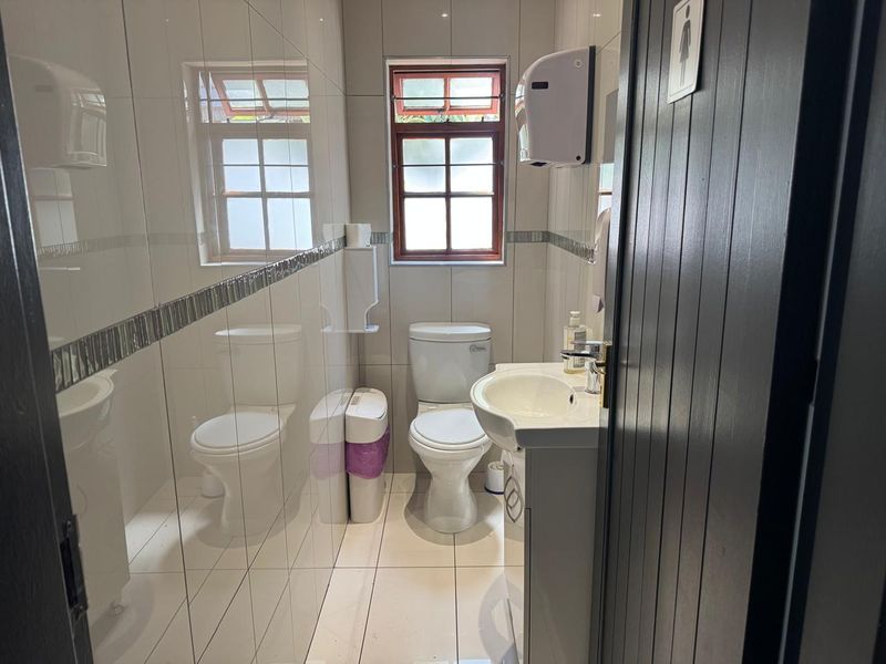 A compact, well-maintained commercial bathroom featuring tiled walls, a pedestal vanity with a washbasin, and a standard toilet.