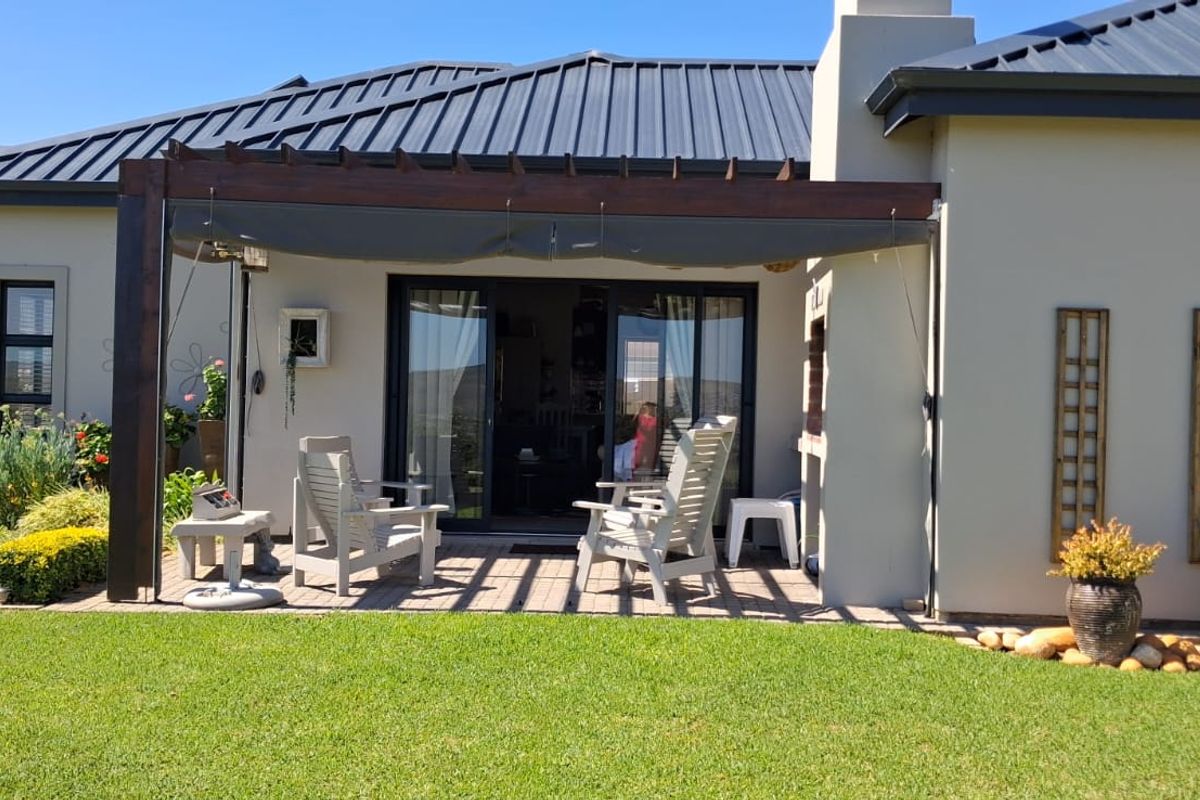 Rear view of the house featuring a paved patio with a wooden pergola, built-in fireplace, and sliding glass doors leading to the interior.