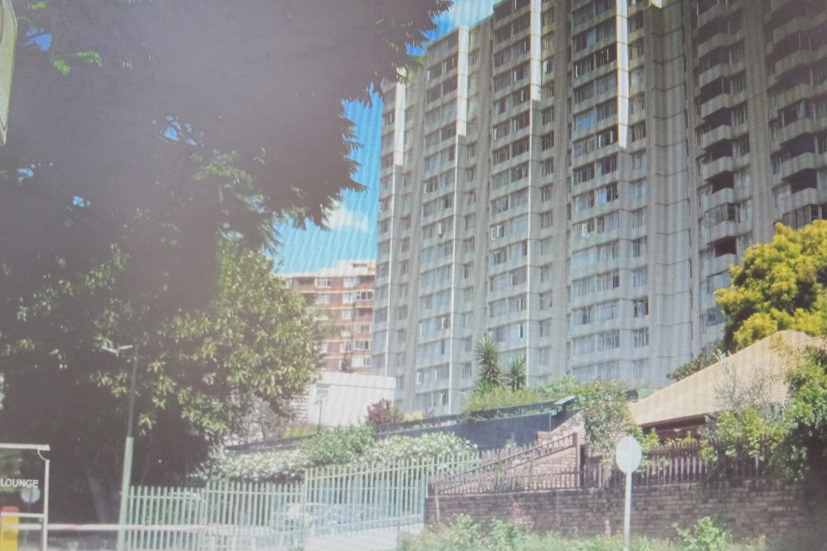 Exterior view of a multi-story apartment building featuring balconies, security fencing, and brick boundary walls.