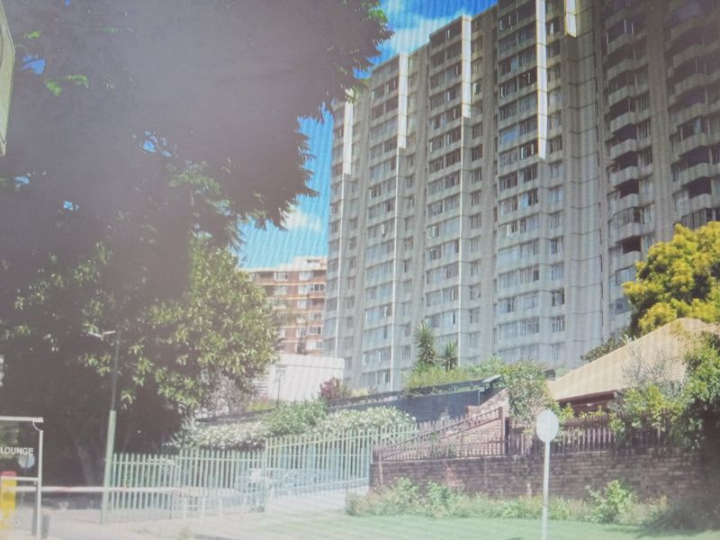 Exterior view of a multi-story apartment building featuring balconies, security fencing, and brick boundary walls.