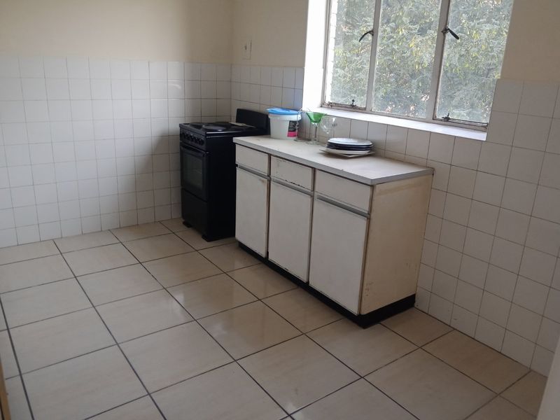 A functional kitchen featuring tiled flooring, a tiled splashback, a freestanding stove, and basic built-in base cabinetry with a laminate countertop.