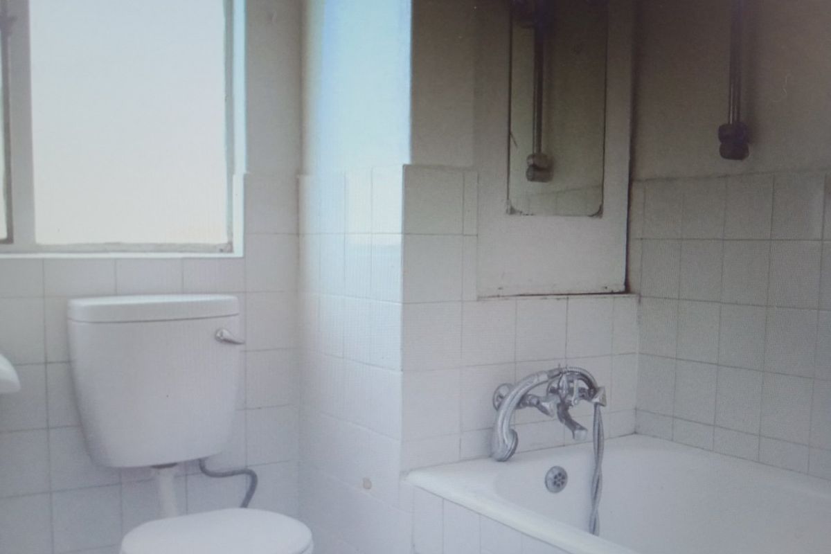 A dated bathroom featuring a standard toilet and bathtub with tiled walls, requiring modernization and cosmetic updates to improve its overall condition.