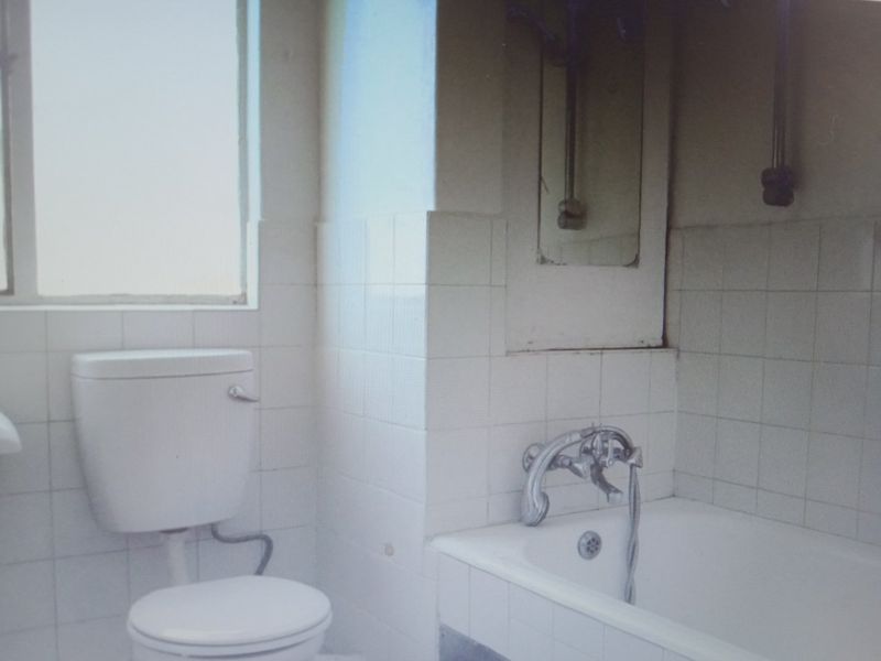 A dated bathroom featuring a standard toilet and bathtub with tiled walls, requiring modernization and cosmetic updates to improve its overall condition.