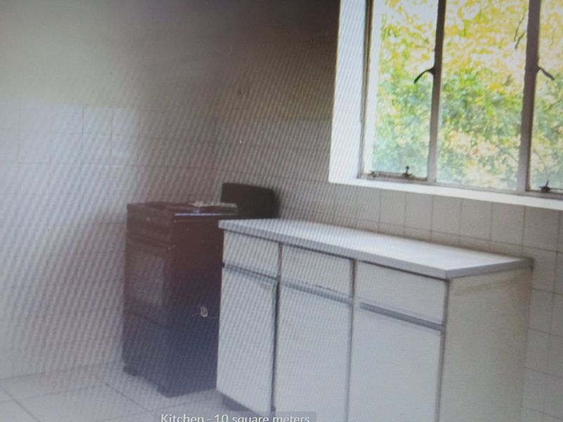 A compact kitchen featuring basic built-in cabinetry, a tiled splashback, and a freestanding stove, offering a functional space ready for modernization.