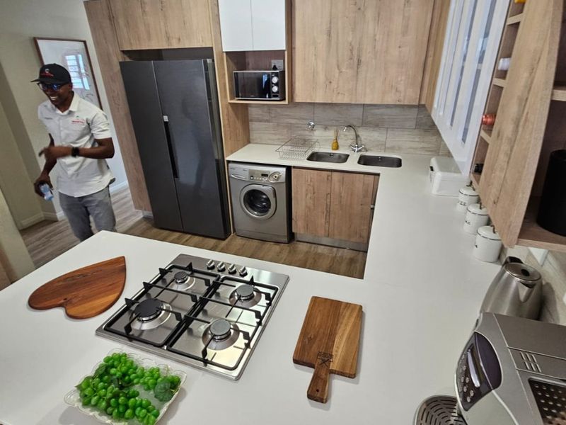 Modern kitchen featuring light wood-tone cabinetry, stone countertops, a gas hob, and integrated appliances including a washing machine and microwave.