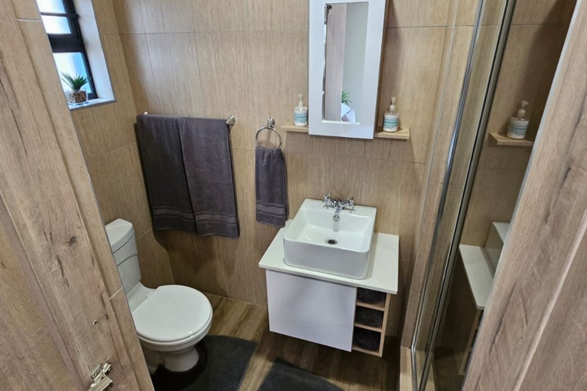 A modern, compact bathroom featuring wood-look wall and floor tiles, a wall-mounted vanity with a vessel sink, and a glass-enclosed shower.