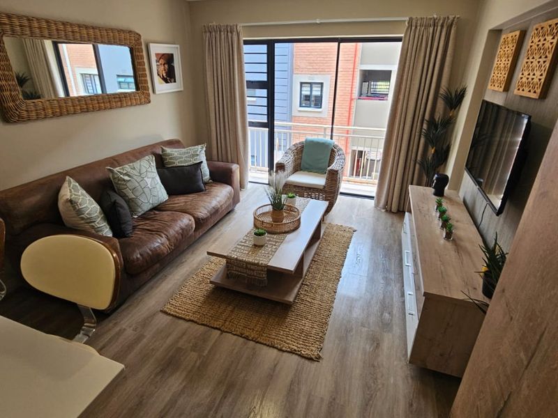 A well-maintained living room featuring modern laminate flooring, neutral wall tones, and a sliding glass door providing access to a private balcony.