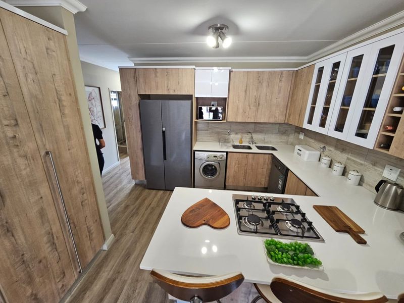 Modern kitchen featuring wood-grain cabinetry, stone countertops, a gas hob, and integrated appliances, offering a functional and contemporary cooking space.