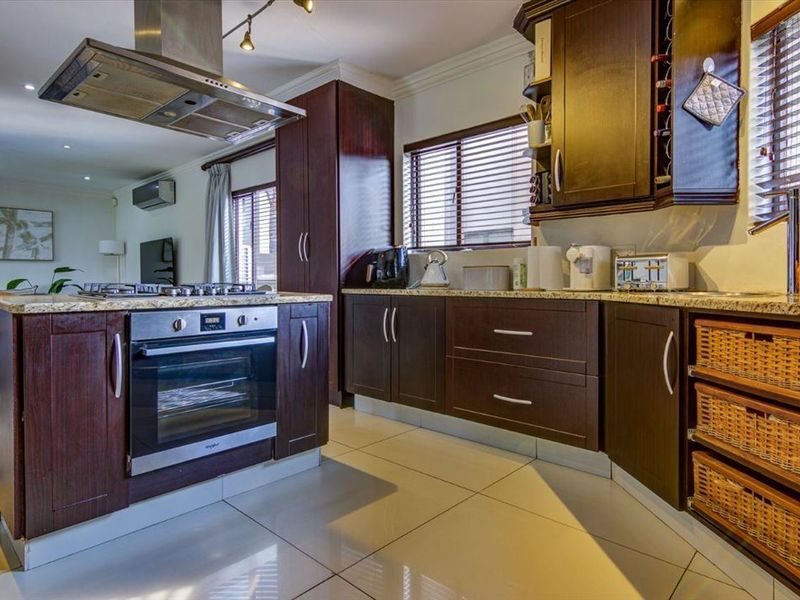 Modern kitchen featuring dark wood cabinetry, granite countertops, built-in oven, gas hob, and stainless steel extractor fan, with tiled flooring throughout.
