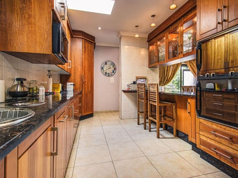 A functional kitchen featuring warm wooden cabinetry, granite countertops, built-in appliances, a breakfast bar, and natural light provided by a skylight.