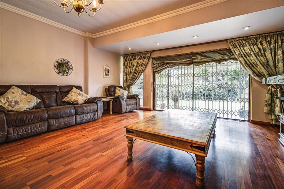 Spacious living room featuring warm laminate flooring, recessed lighting, and large sliding glass doors with security gates providing access to the garden.