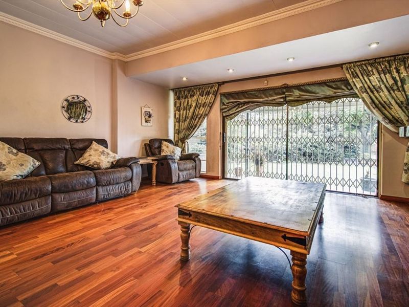 Spacious living room featuring warm laminate flooring, recessed lighting, and large sliding glass doors with security gates providing access to the garden.