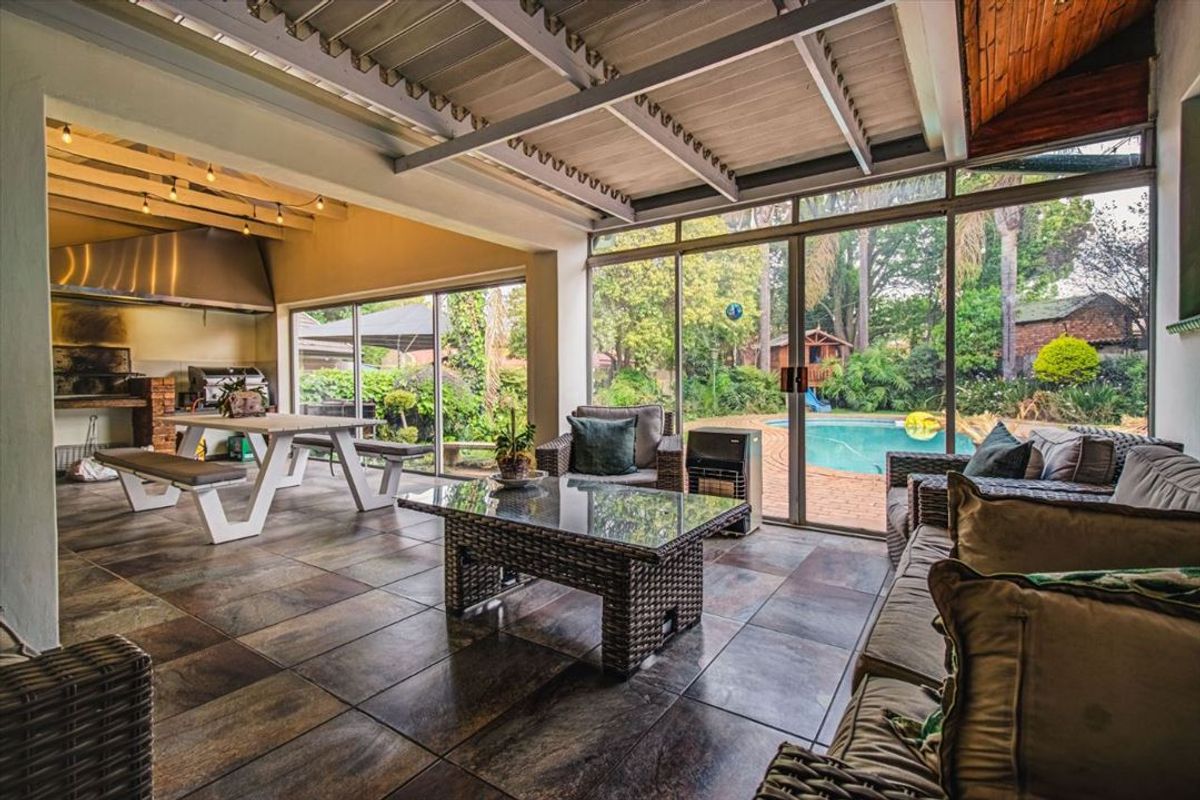 Spacious covered patio featuring a built-in braai, stainless steel extractor, tiled flooring, and large sliding glass doors overlooking the garden and pool area.