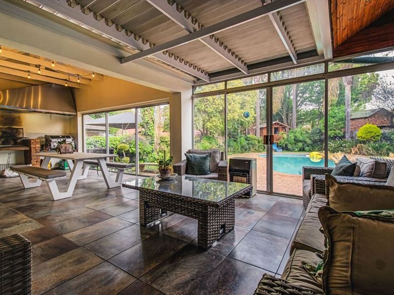 Spacious covered patio featuring a built-in braai, stainless steel extractor, tiled flooring, and large sliding glass doors overlooking the garden and pool area.