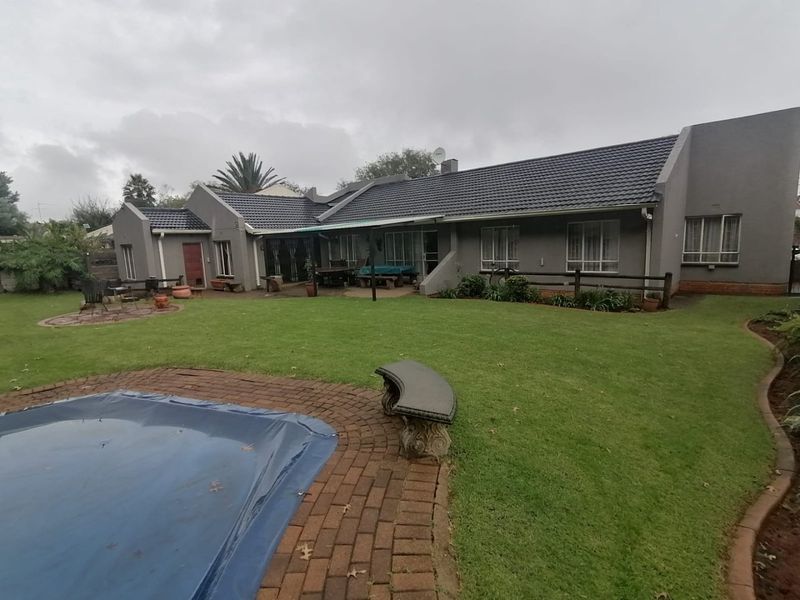 Rear view of the property featuring a spacious lawn, swimming pool with brick surround, and a covered patio area attached to the main dwelling.